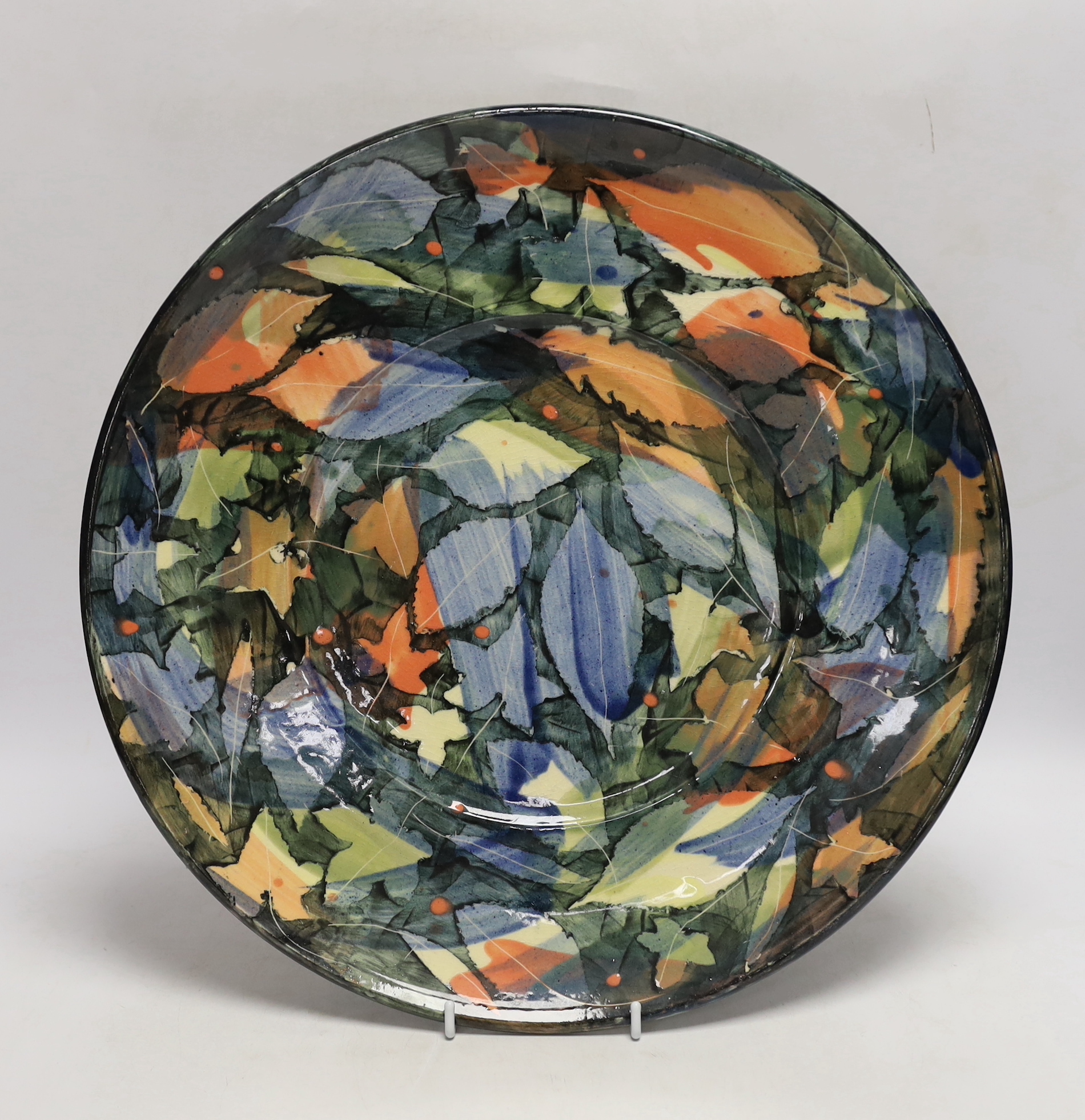 A large studio pottery plate by Sophie McCarthy, decorated with a variety of autumnal leaves, signed to the base, 39.5cm
